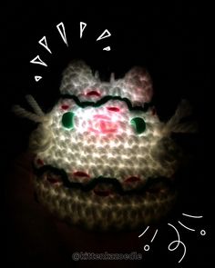 a white crocheted cake with green eyes on it's face in the dark