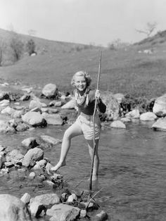 an old photo of a woman standing on rocks in the water holding onto a pole