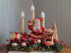 a christmas centerpiece with candles, ornaments and a santa clause figure on the table