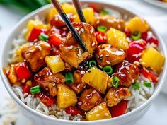 a white bowl filled with pineapple chicken over rice and chopsticks in it