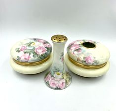 three pieces of porcelain with flowers painted on the sides and gold trimming around them