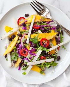 a white plate topped with a salad covered in cheese and black olives next to a fork