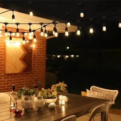 an outdoor dining area with lights strung from the ceiling and table set for two, surrounded by white wicker chairs