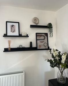 two black shelves with pictures and flowers on them in a room next to a radiator