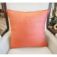 an orange pillow sitting on top of a white chair next to a vase with flowers