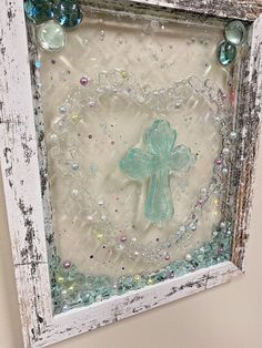 an old frame with glass beads and a small green cross on it is hanging on the wall