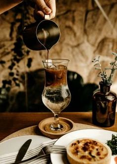 a person pouring something into a glass on top of a white plate with silverware