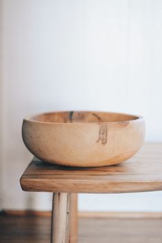 a wooden bowl sitting on top of a wooden table next to a white wall and wood floor