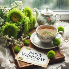 a cup of tea and some flowers on a table with a sign that says happy wednesday