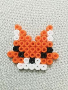 an orange and white cat made out of plastic beads on a gray surface with black dots