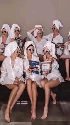 a group of women sitting on top of a couch wearing white robes and holding books