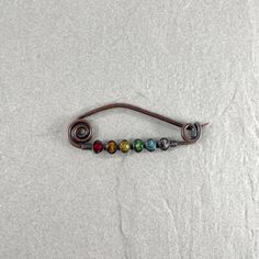 a metal hook with seven different colored beads on it's end, sitting on a white surface