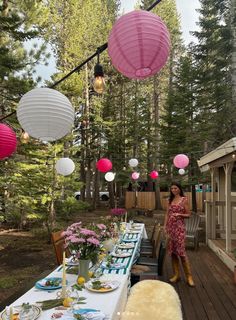 a woman standing next to a table with plates and cups on it in the woods