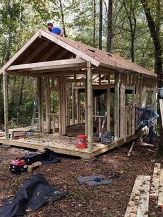 a small wooden building in the woods with people working on it's roof and windows