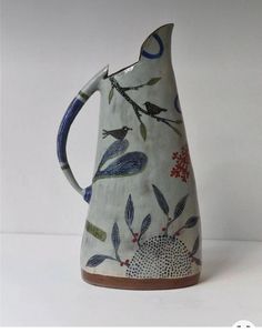 a ceramic pitcher with birds and flowers on it's side, sitting on a white surface