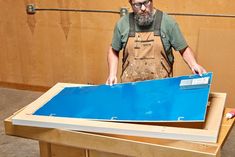 a man in overalls working on a blue piece of wood