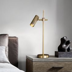 a gold lamp on a nightstand next to a bed with pillows and a black sculpture