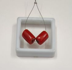 two red heart shaped beads hanging from a white square frame on a wall ornament