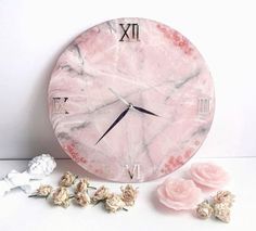 a pink marble clock sitting on top of a white table next to flowers and petals