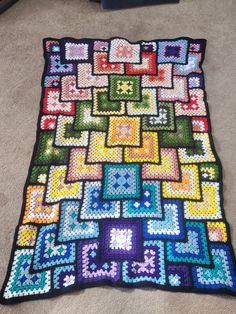 a crocheted blanket is laying on the floor in front of a carpeted area