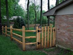 a wooden fence in front of a brick building with trees and grass on the other side