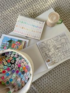 there are many different colored buttons on the table next to a cup of coffee and a coloring book