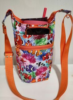 an orange strap is attached to a multicolored floral purse with cell phone in it