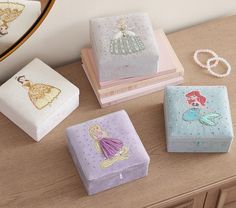 four princess jewelry boxes sitting on top of a wooden table next to a mirror and beaded bracelets