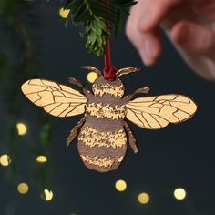 a hand holding a christmas ornament with a bee hanging from it's side