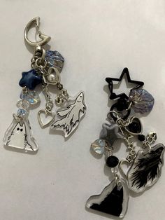 two key chains with charms attached to them on a white surface, one has an angel and the other is a ghost