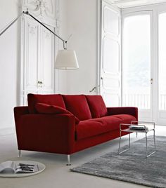 a red couch sitting on top of a white floor next to a lamp and rug