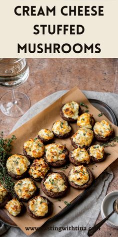 cream cheese stuffed mushrooms on a tray with wine glasses and utensils in the background