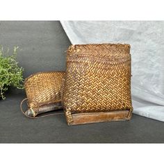 two woven baskets sitting next to each other on top of a black surface with a plant in the background