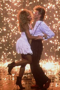 a man and woman dancing in front of a firework display with their arms around each other