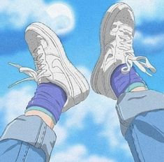 someone's feet with blue jeans and sneakers on, standing in front of the sky