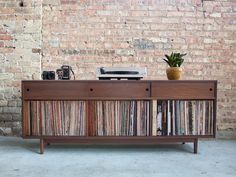 an old record player sitting on top of a wooden cabinet next to a brick wall