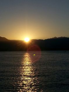 the sun is setting over water with mountains in the background