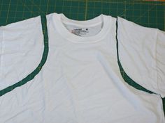 a white t - shirt is laying on a green cutting mat with scissors and tape