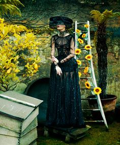 a woman wearing a black dress and hat standing in front of sunflowers