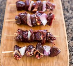 several skewered meats and onions on a wooden cutting board