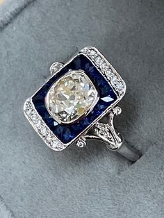 ART DECO RING with a 1.48ct Old Mine Brilliant center diamond . The ring is a newer mounting made with 1.15ct of natural blue sapphires custom cut to fit around the center diamond. There are also .15ct of small accent diamonds going down the detailed sides of the ring. Wonderfully crafted. A blend of old and new. Finger Size 6.5 in 14k White gold. ALL NATURAL DIAMONDS. NOT LAB GROWN. Art Deco Sapphire Ring, Deco Ring, Antique Engagement Rings, Natural Blue Sapphire, Fantasy Jewelry, Art Deco Ring, Vintage Diamond, Jewelry Ideas, Lab Grown