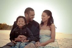 a man, woman and child are sitting on the beach with their arms around each other