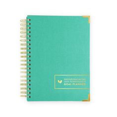 a green spiral notebook with gold trim on the front and bottom cover, sitting open