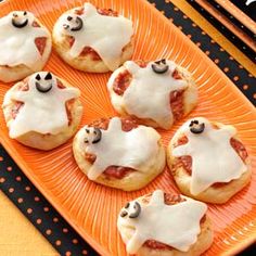 small pizzas with white icing and black eyes on an orange plate next to halloween decorations