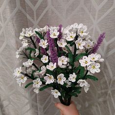 a hand holding a bouquet of white and purple flowers