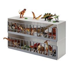 several toy dinosaurs in a metal container on top of a white table with two people looking at them