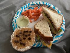 a plate with a sandwich, carrots and peanut butter on it