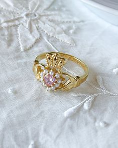 a gold ring with pink and white stones on it sitting on a lace tablecloth