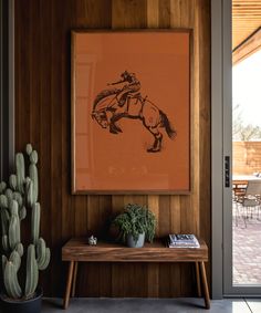 a painting hangs on the wall next to a table with a cactus and potted cacti