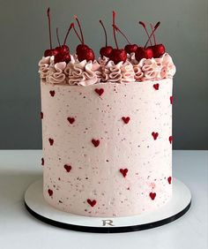 a white cake with pink frosting and red hearts on the top, topped with cherries